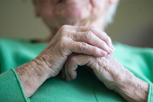 Eine Seniorin steht am Fenster und schaut hinaus.