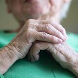 Eine Seniorin steht am Fenster und schaut hinaus.
