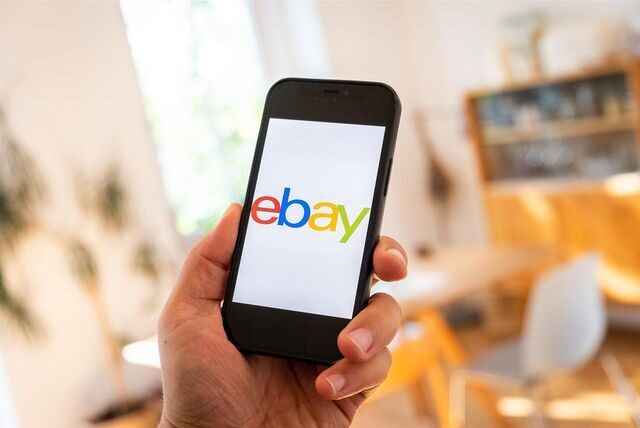 Eine Hand, die ein Smartphone hält. Auf dem Display steht „ebay“ in bunten Buchstaben.