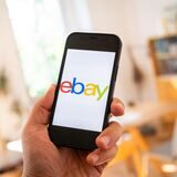 Eine Hand, die ein Smartphone hält. Auf dem Display steht „ebay“ in bunten Buchstaben.