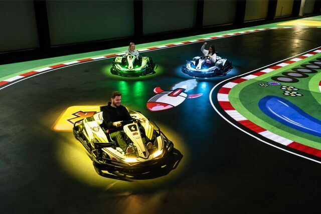 Drei Menschen fahren bei BattleKart mit Karts über die LED-Strecke.