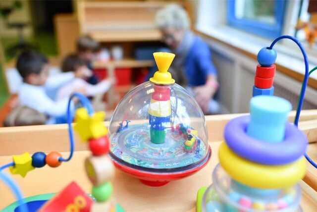 Spielgeräte im Vordergrund und eine Erzieherin und Kinder im Hintergrund