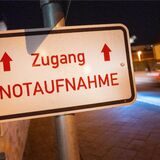 Ein weißes Schild mit roter Schrift an einem Pfahl. Darauf steht „Zugang. Notaufnahme.“