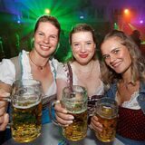 Drei Frauen im Dirndl strecken ihr Bier in die Kamera und lächeln herzlich