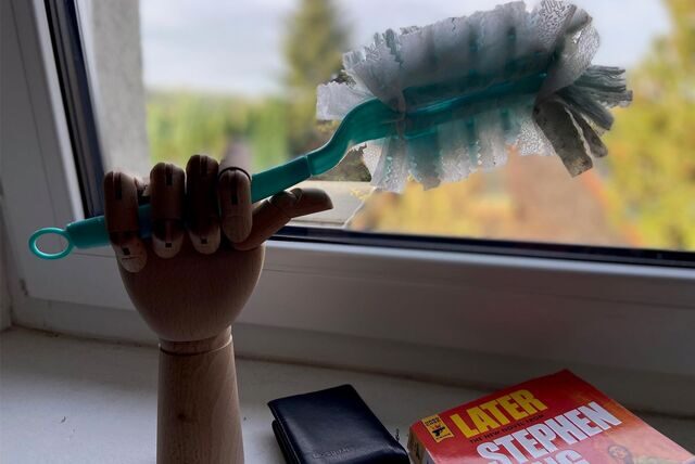 Eine hölzerne Hand hält einen Staubwedel.