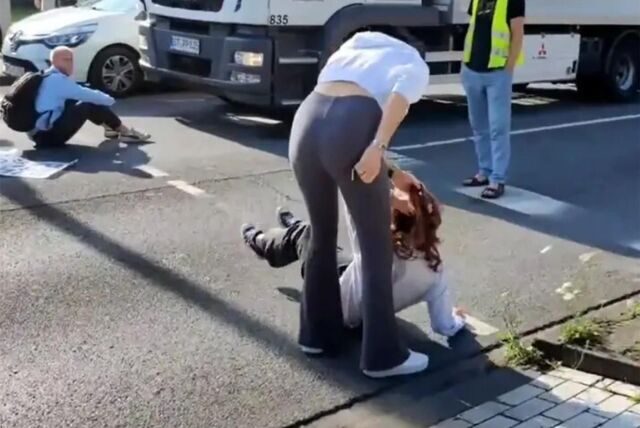 Eine Passantin zerrt eine Klimakleberin an den Haaren von der Straße