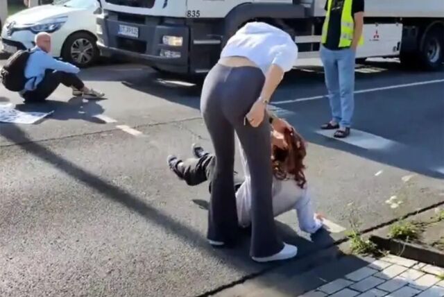 Eine Passantin zerrt eine Klimakleberin an den Haaren von der Straße