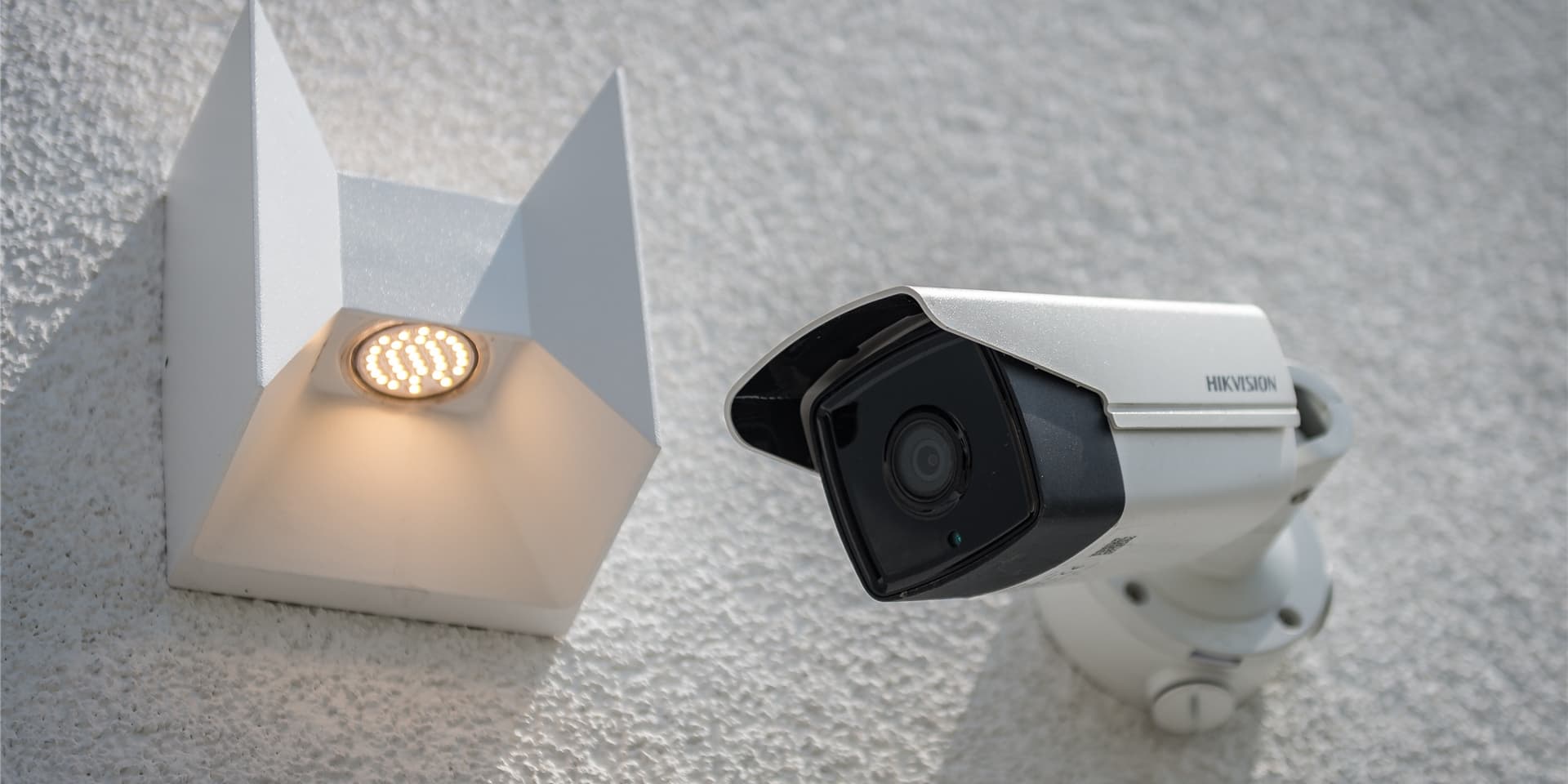 Eine Videokamera hängt neben einem Außenlicht an der Hausfassade