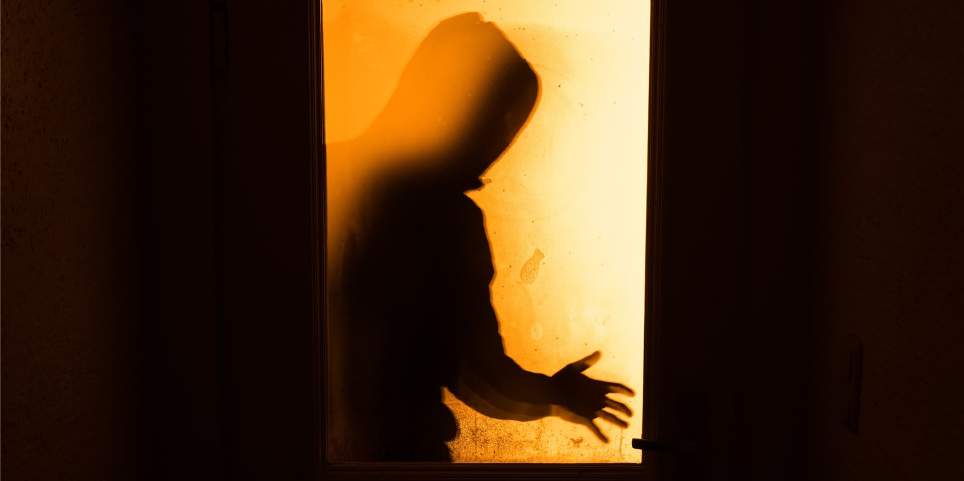 Die Silhouette eines Mannes durch ein beleuchtetes Fenster.