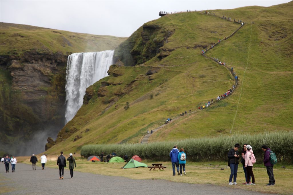 title attribut Touristen spazieren am Wasserfall Skogafoss vorbei. Jahrelang sind die Touristenzahlen auf Island in die Höhe geschossen. Jetzt sollte sich all das stabilisieren. Stattdessen kam Corona - mit immensen Folgen für die isländische Reisebranche.