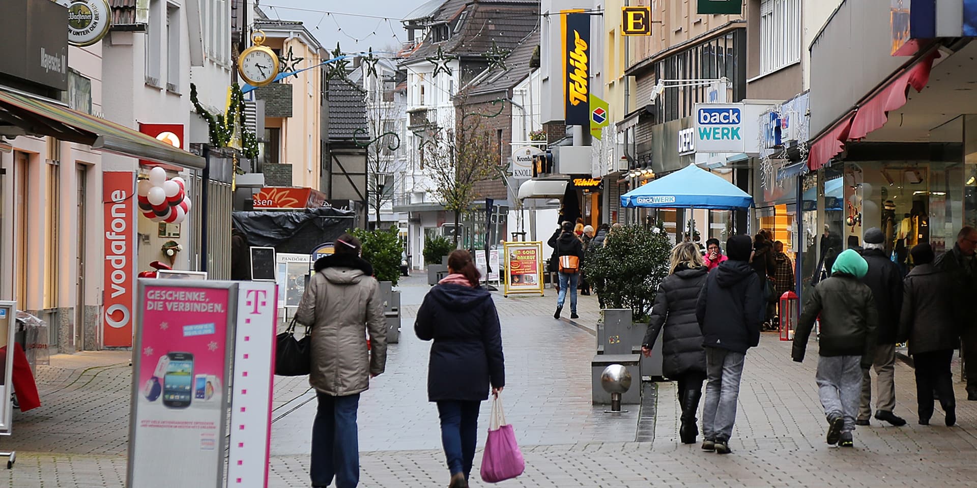 Eine Einkaufsstraße ist zu sehen. Ladenschilder weisen auf Geschäfte hin. In der Fußgängerzone spazieren Menschen. (Archivbild)