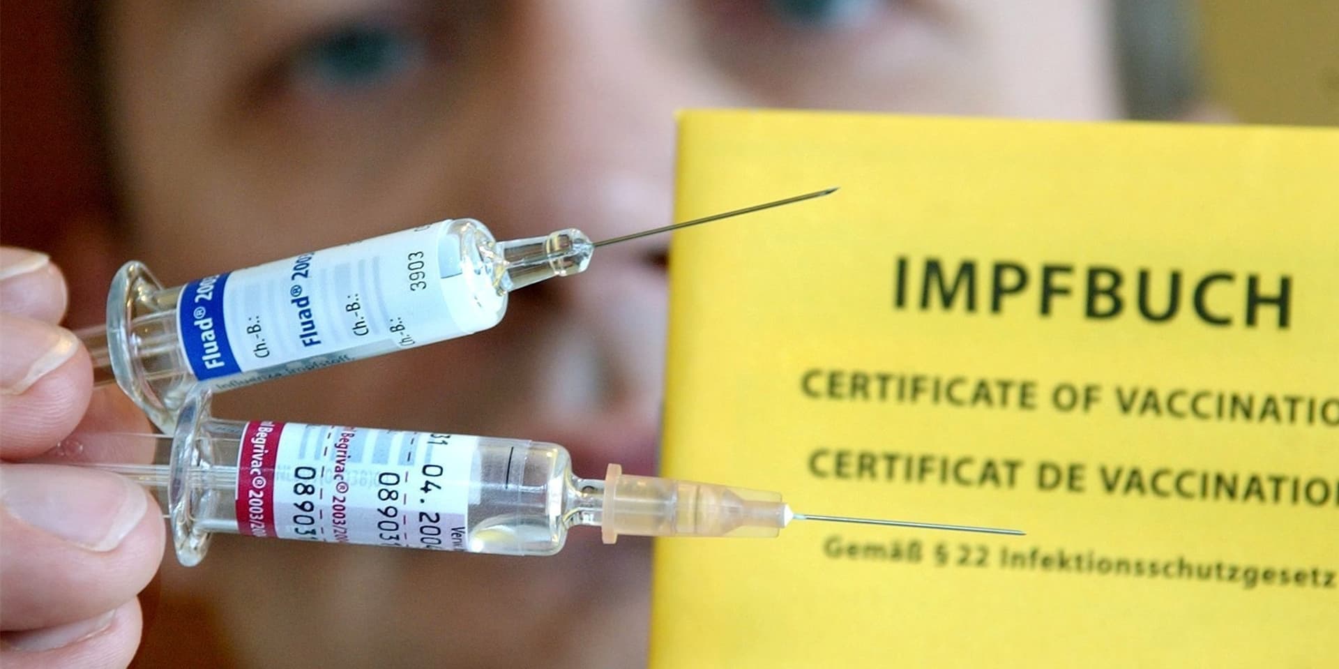 Mann hält zwei Spritzen mit Grippe-Impfstoff und ein Impfbuch hoch