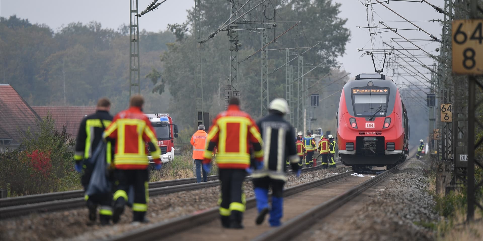 Rettungskräfte und ein Feuerwehrauto neben Bahngleisen mit Zug (Symbolbild).