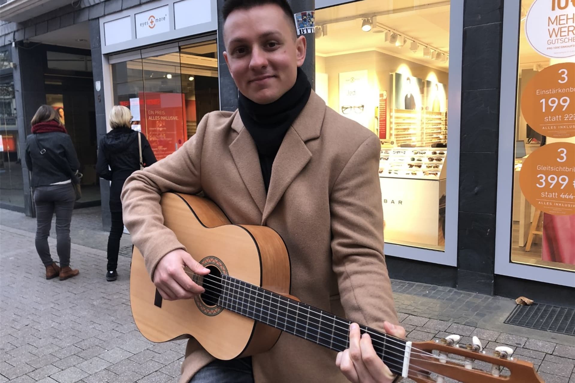 Kim Friehs steht mit seiner Gitarre vor einem Laden.