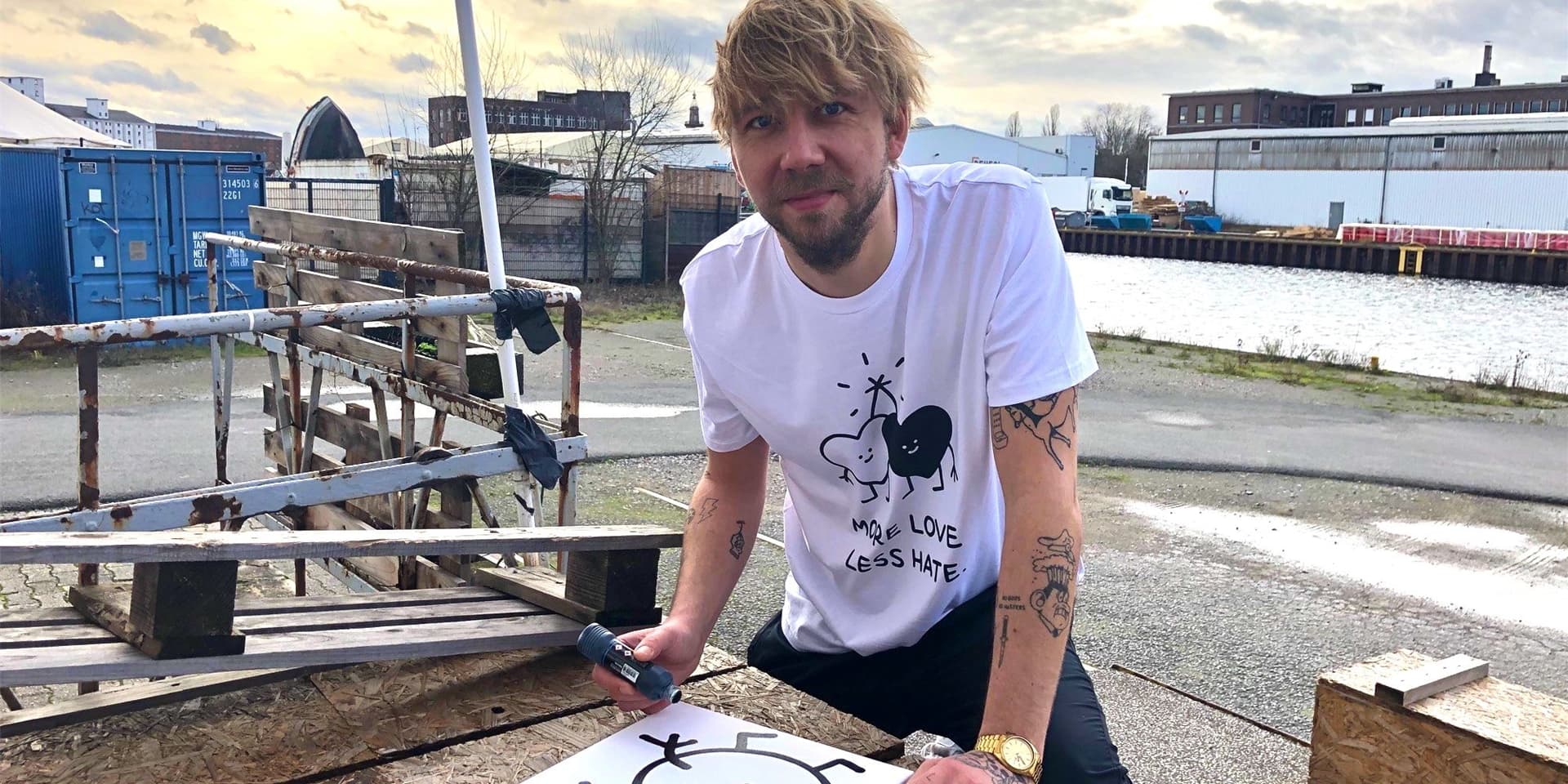 Der Künstler Alex Zimmermannin in typischer Aktion am Hafen. Das T-Shirt mit seinem Motiv „More Love, Less Hate“ ist dabei gut zu erkennen.