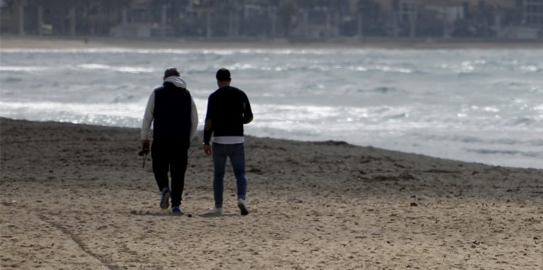 Zwei Männer gehen am Strand von Arenal über den Sand.