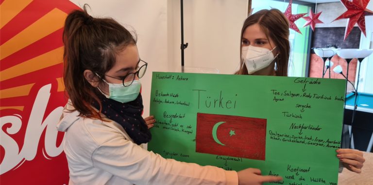 Avsin (links) erklärt, dass sich die Türkei auf den Kontinenten Asien und Europa befindet. Sprachlernbegleiterin Carina Eller hält das Plakat.