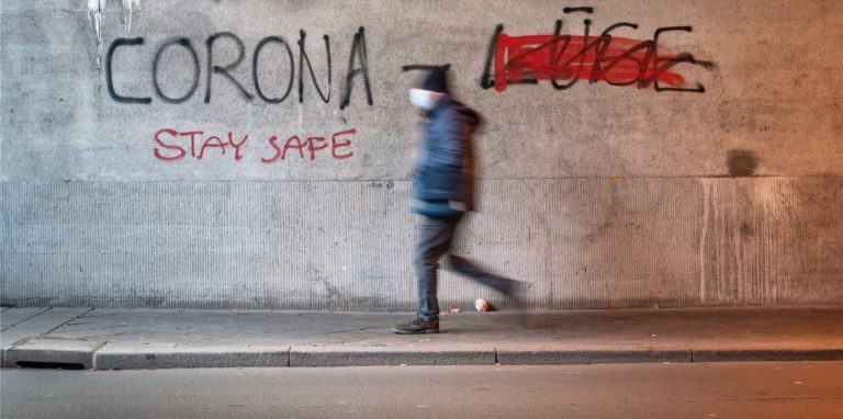 Ein Mann mit Mund-Nasen-Schutz geht durch eine Eisenbahnunterführung, an deren Wand «Corona Lüge» geschrieben steht, wobei mit roter Farbe das gesprühte Wort «Lüge» (r) durchgestrichen wurde.