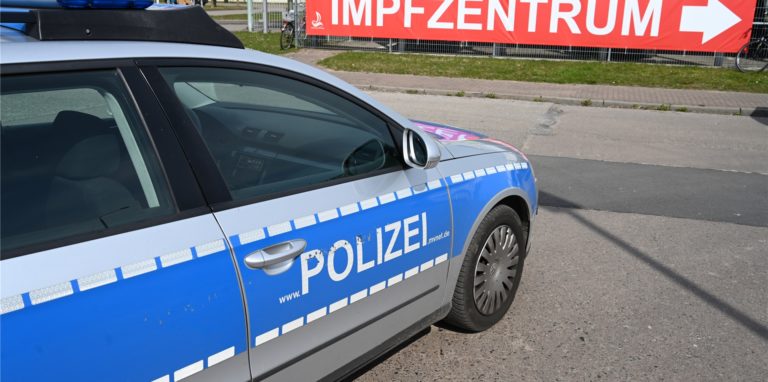 Ein Polizeiauto steht vor einem Schild mit dem Schriftzug „Impfzentrum“.
