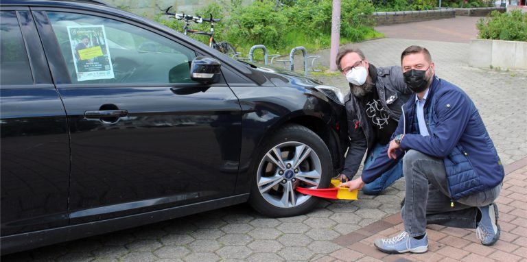 Stadtradelkoordinator Frank Hugo (l.) legt mit der Parkkralle das Auto von Jens Toschläger an die Kette. Unnas Technischer Beigeordneter ist in diesem Jahr der offizielle Botschafter des Stadtradelns. In dieser Funktion will er tatsächlich drei Wochen lang auf seinen Wagen verzichten.