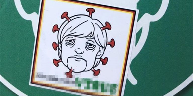 Der Aufkleber auf einem Corona-Hinweisschild in der Lüner Innenstadt stellt Bundeskanzlerin Angela Merkel als Virus dar. Wir haben den entsprechenden Schriftzug unter dem Kopf unkenntlich gemacht, um die Botschaft nicht weiter zu verbreiten.