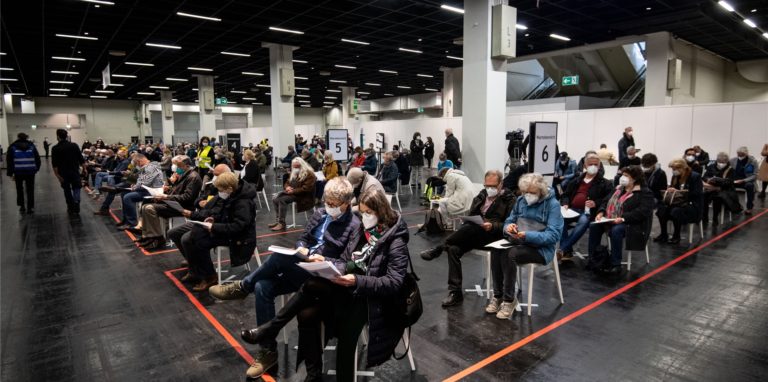 Menschen warten mit Mund-Nasen-Bedeckung in einem Impfzentrum. Die Terminvergabe für die Impfzentren wird in NRW für alle Impfwilligen freigegeben.