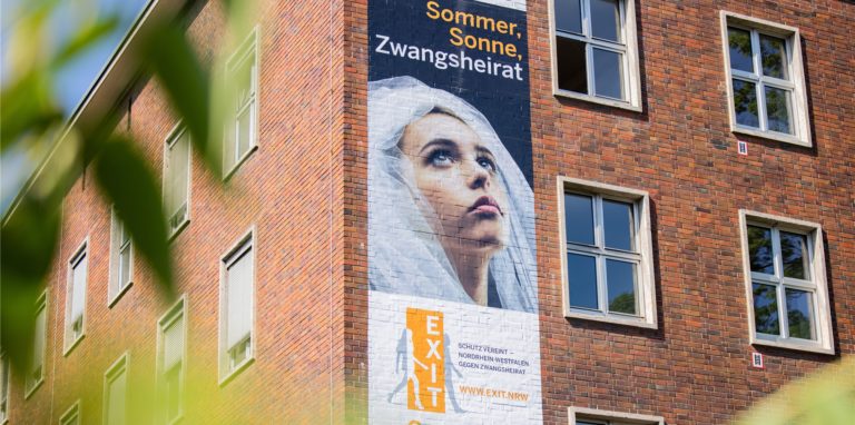 Ein Plakat mit der Aufschrift „Sommer, Sonne, Zwangsheirat“ hängt am Ministerium für Heimat, Kommunales, Bau und Gleichstellung des Landes Nordrhein-Westfalen. Netzwerk aus Unna warnt vor der Ferien vor Ehe-Tourismus.