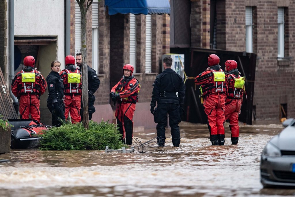 title attribut Rettungsschwimmer und Polizeitaucher stehen in einer überfluteten Straße im Ortsteil Blessem.