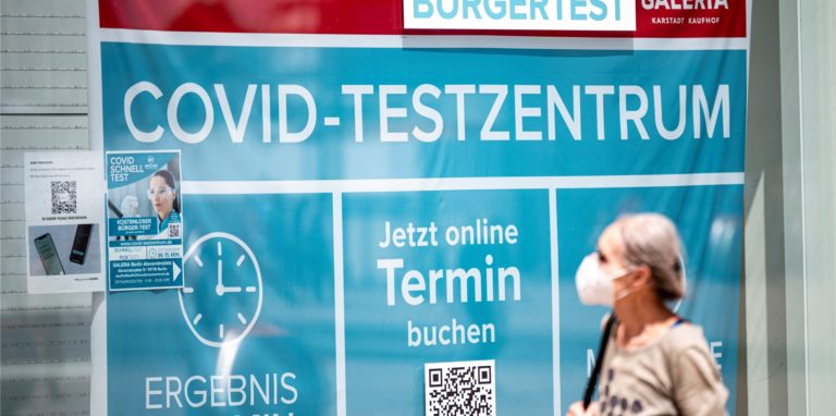Eine Frau mit Maske läuft an einem Corona-Testzentrum vorbei. (Symbolbild)
