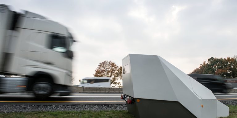 Ein Enforcement Trailer zur Überwachung der Geschwindigkeit steht an einer Autobahn. Autos und Lastwagen fahren daran vorbei