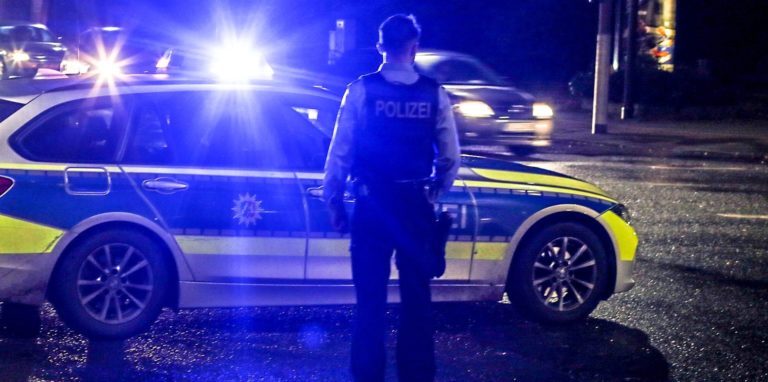 Polizei steht nachts vor Einsatzwagen mit Blaulicht (Symbolbild)