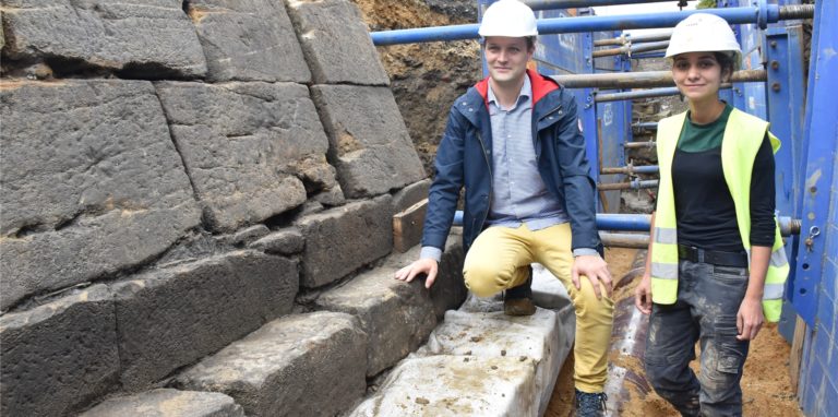 Stadtarchäologe Ingmar Luther und Grabungsleiterin Noelia Madrigal stehen neben einem Strebpfeiler der historischen Stadtmauer.