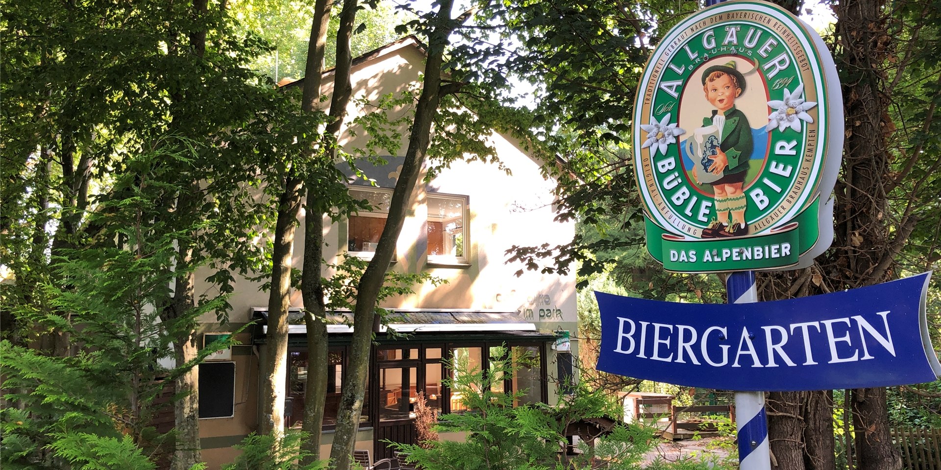 Zwischen Bäumen steht im Kurpark in Unna-Königsborn das Gebäude des Bistros. Davor steht ein Schild mit der Aufschrift „Biergarten“.