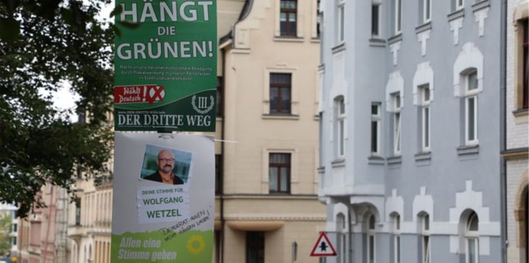 Ein umstrittenes Wahlplakat der Splitterpartei „III Weg“ hängt über einem Plakat der Grünen.