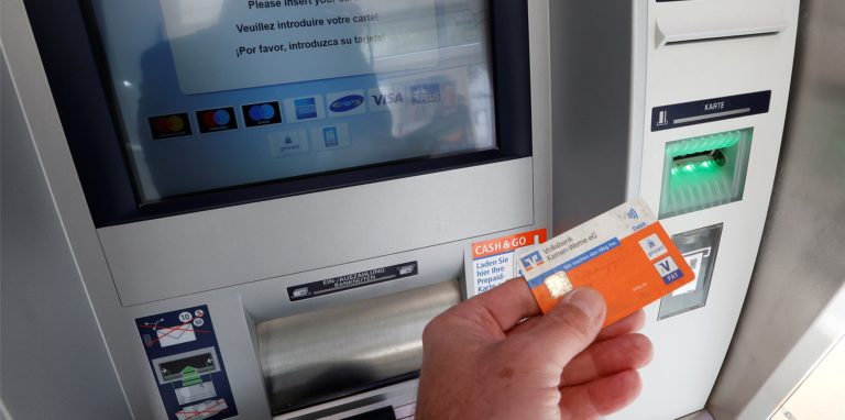 Ein Hand hält eine EC-Karte vor einem Geldautomaten der Volksbank.