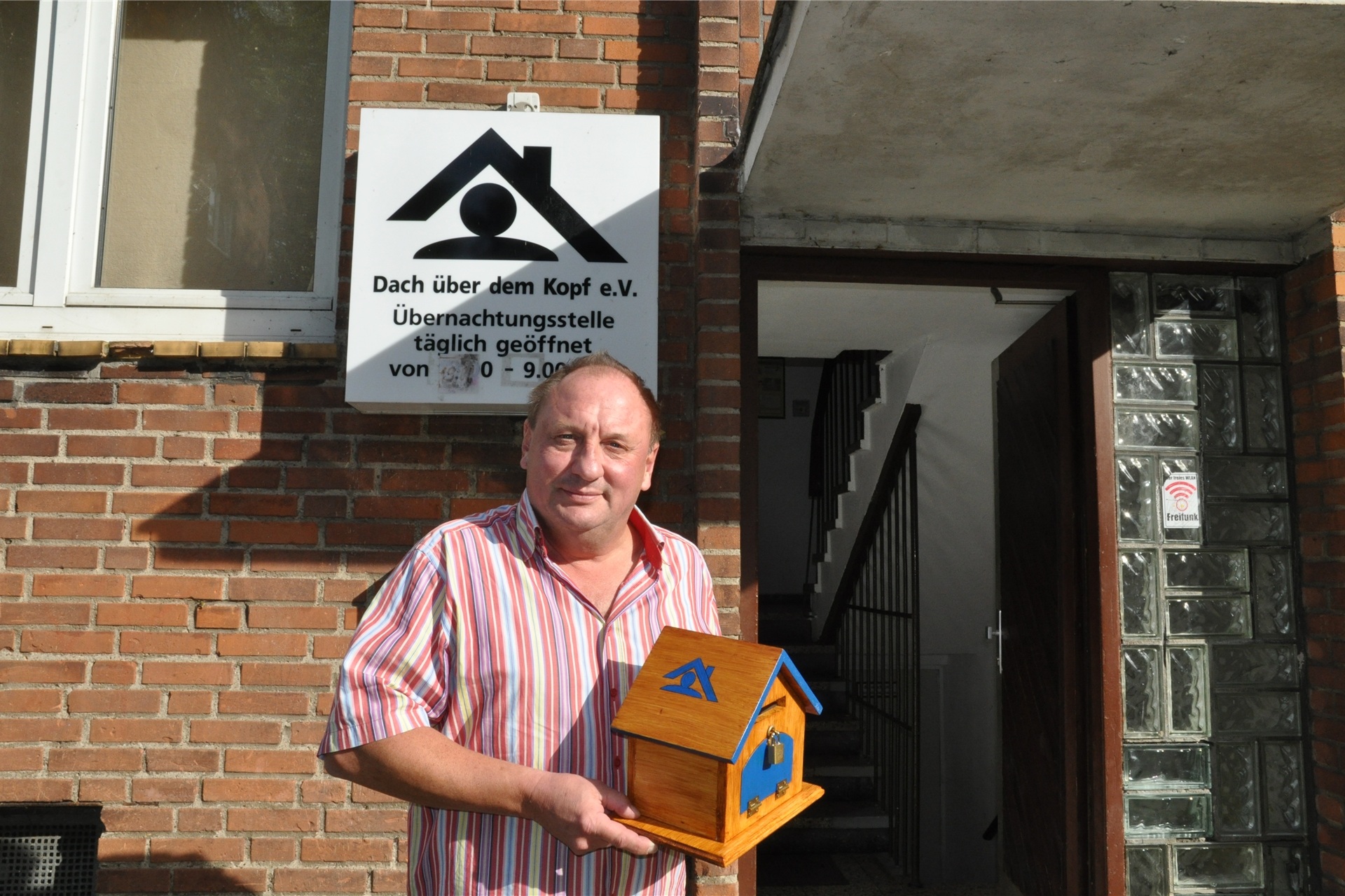 Ein Mann steht vor einem Haus und hält ein Vogelhaus in der Hand.