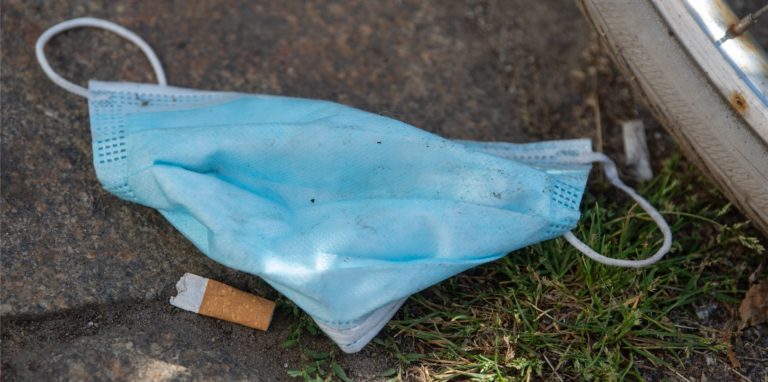 Eine weggeworfene Maske liegt auf dem Fußweg vor einem Supermarkt.
