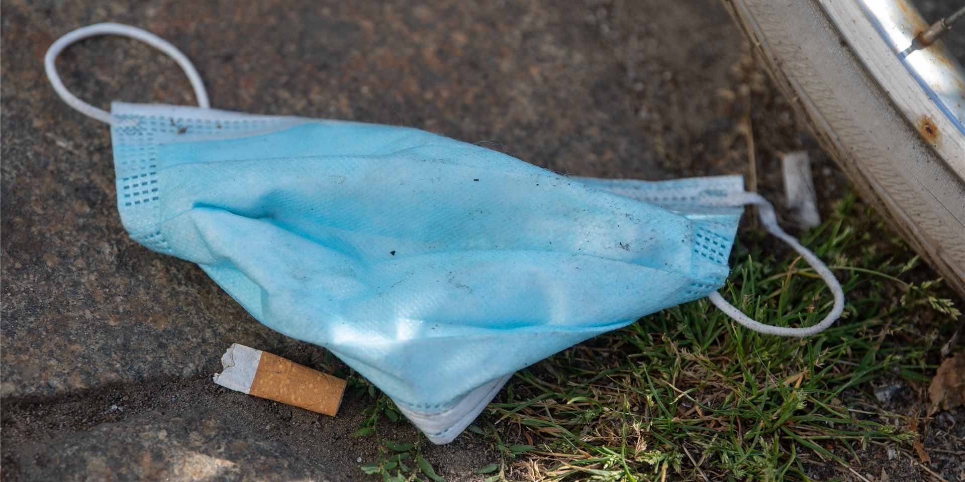 Eine weggeworfene Maske liegt auf dem Fußweg vor einem Supermarkt.
