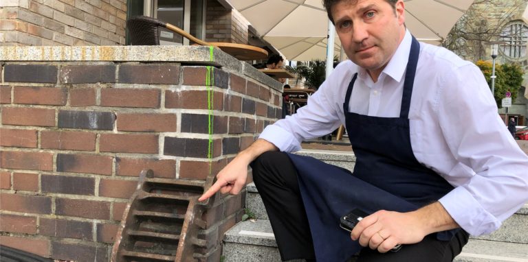 Einbruch mit roher Gewalt: Roberto Cardia zeigt den Gullydeckel, mit dem ein Unbekannter eine Scheibe seiner Eisdiele eingeworfen hat.