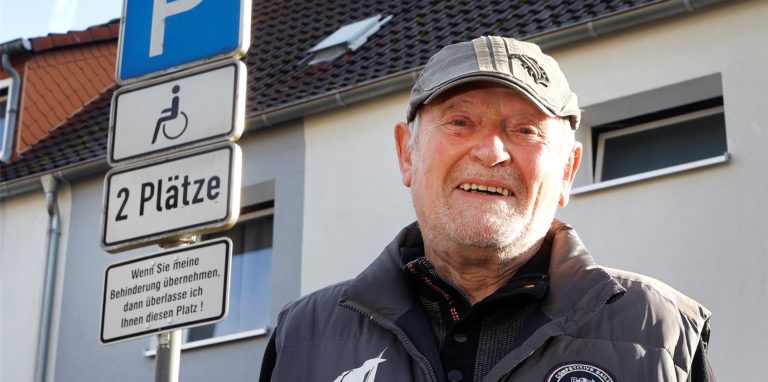 Manfred Grod, Geschäftsführer der Kreisverkehrswacht Unna, steht an der Ebertstraße in Bergkamen vor einem von ihm initiierten Schild, auf dem die Bedeutung von Behindertenparkplätzen unterstrichen wird.