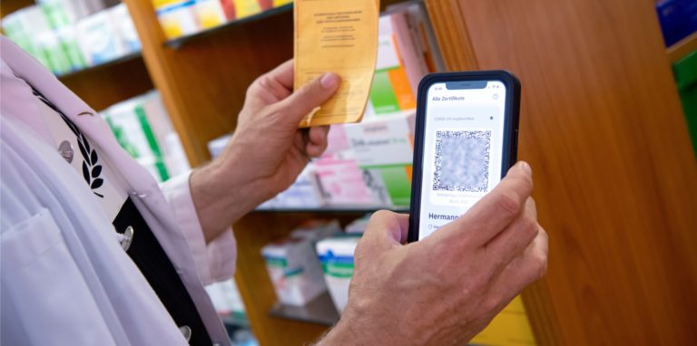 Ein Apotheker hält einen Impfpass und einen digitalen Impfnachweis in den Händen. Immer mehr Apotheker klagen inzwischen über gefälschte Impfausweise. Auch in Schwerte gab es schon Versuche.
