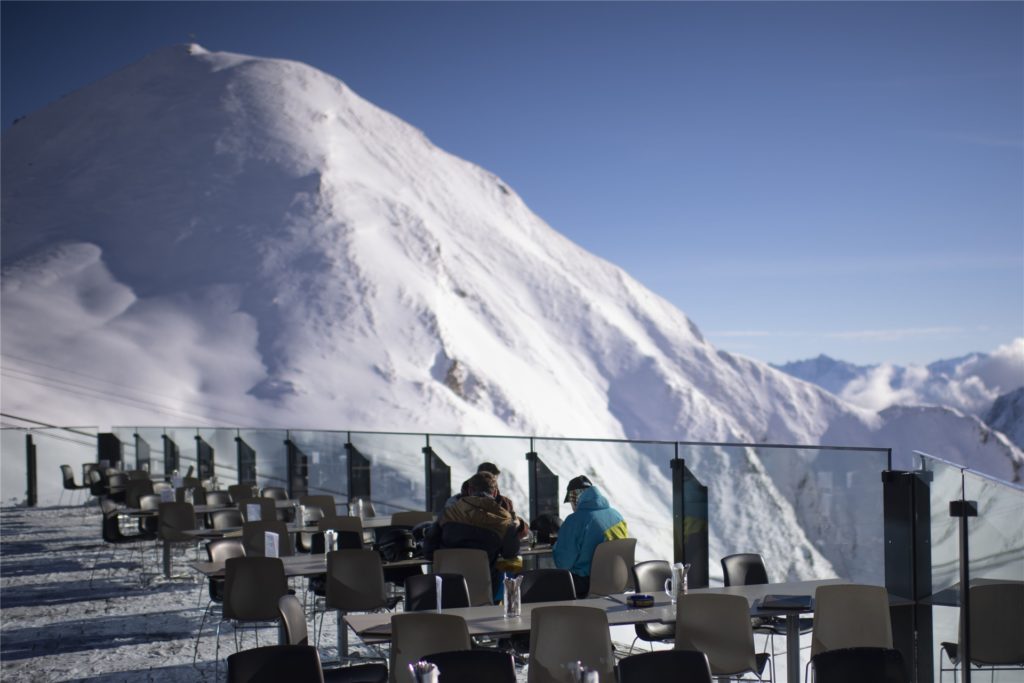 title attribut Gäste sitzen auf der Terrasse eines Bergrestaurants im Skigebiet Silvretta Arena in Samnaun. Das Schweizer Samnaun betreibt mit Ischgl in Tirol (Österreich) ein gemeinsames Skigebiet.