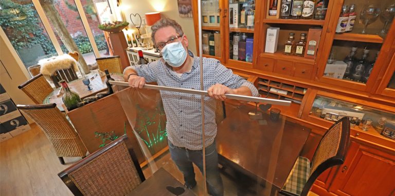 Christian Plischke, Mitinhaber des Feinkost-Bistros Refugio in Unna, baut einen transparenten Aufsteller als Corona-Schutz auf.