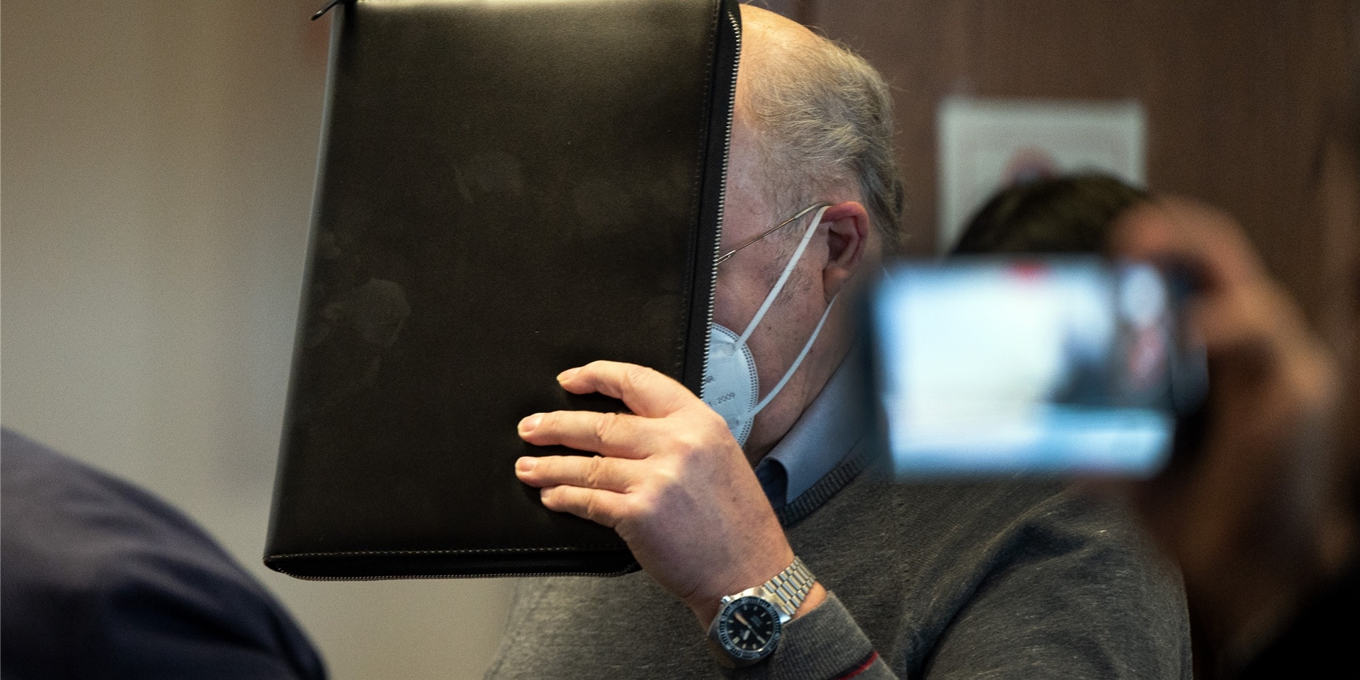 Der angeklagte katholische Priester hält sich im Gerichtssaal eine Mappe vor das Gesicht. Er wird wegen sexuellen Missbrauchs angeklagt. Der 70-Jährige soll in den 1990er Jahren in 31 Fällen seine damals zwischen 7 und 13 Jahre alten Nichten missbraucht haben.