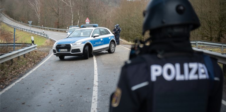 Polizeibeamte stehen an einer Absperrung an der Kreisstraße 22 rund einen Kilometer von dem Tatort, an dem zwei Polizeibeamte durch Schüsse getötet wurden.