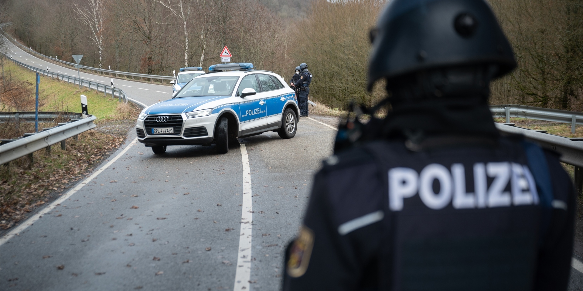 Polizeibeamte stehen an einer Absperrung an der Kreisstraße 22 rund einen Kilometer von dem Tatort, an dem zwei Polizeibeamte durch Schüsse getötet wurden.