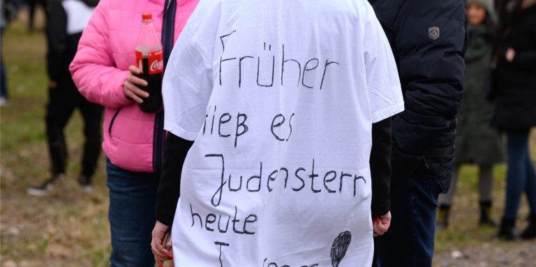 Eine Frau trägt während einer Kundgebung der „Querdenken“-Bewegung ein T-Shirt mit der Aufschrift „Früher hieß es Judenstern, heute Impfpass“.