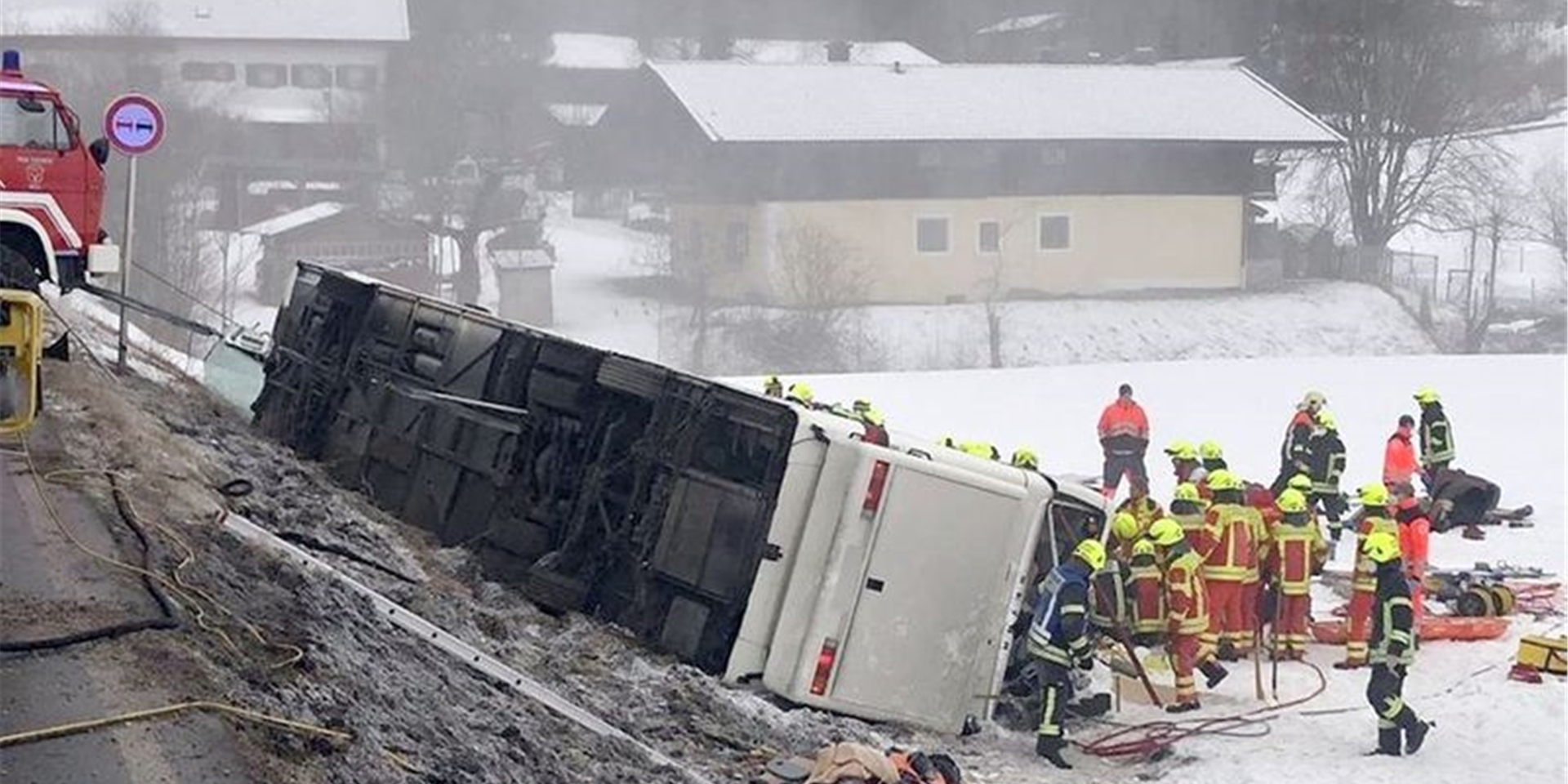 Einsatzkräfte der Feuerwehr stehen neben einem umgekippten Reisebus am Straßenrand.