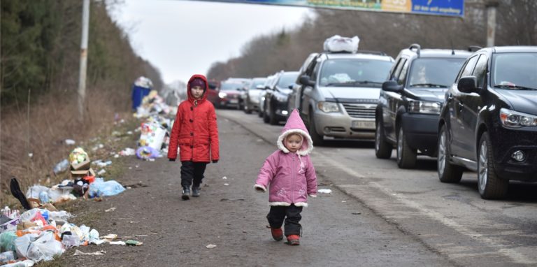 Kinder gehen an einer Autoschlange vorbei, die auf dem Weg zur polnischen Grenze ist. Auch in Schwerte werden bald mehr Flüchtlinge aus der Ukraine eintreffen. Der Arbeitskreis Asyl sucht deshalb nach Paten. Besonders Familien können helfen.