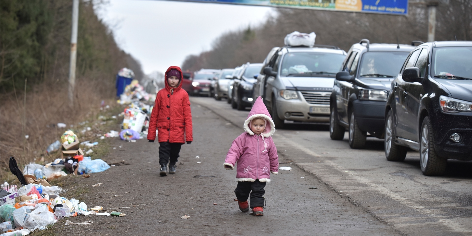Kinder gehen an einer Autoschlange vorbei, die auf dem Weg zur polnischen Grenze ist. Auch in Schwerte werden bald mehr Flüchtlinge aus der Ukraine eintreffen. Der Arbeitskreis Asyl sucht deshalb nach Paten. Besonders Familien können helfen.